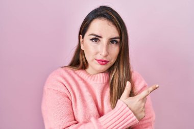 Pembe arka planda duran genç İspanyol kadın, elini kenarı işaret ediyor, ciddi ve sakin bir yüz ifadesi sergiliyor. 