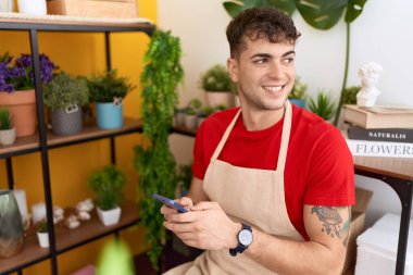 Çiçekçide akıllı telefon kullanarak gülümseyen İspanyol çiçekçi.