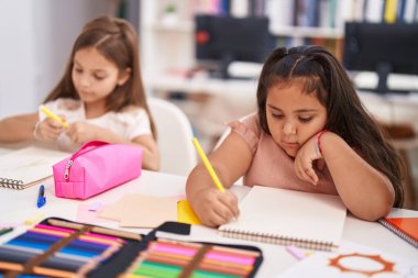 Two kids preschool students sitting on table drawing on paper at classroom