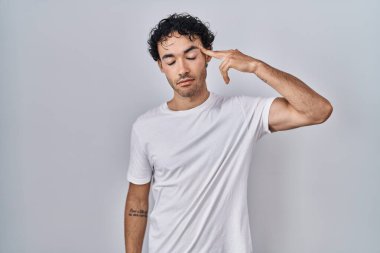 Hispanic man standing over isolated background shooting and killing oneself pointing hand and fingers to head like gun, suicide gesture. 