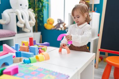 Adorable blonde girl playing with toys standing at kindergarten