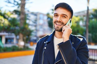Genç İspanyol adam gülümsüyor. Parktaki akıllı telefondan konuşuyor.