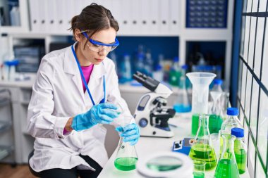 Genç ve güzel İspanyol bilim kadını laboratuarda test tüpüne sıvı döküyor.