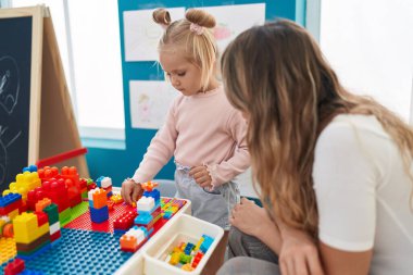 Teacher and toddler playing with construction blocks sitting on table at kindergarten