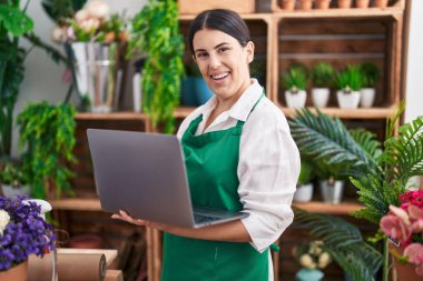 Young beautiful hispanic woman florist smiling confident using laptop at flower shop
