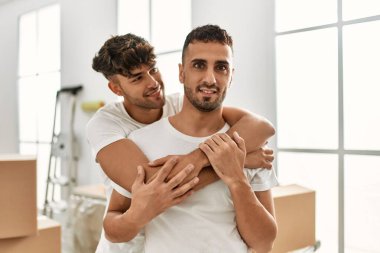 Two hispanic men couple smiling confident hugging each other standing at new home