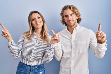 Young couple standing over blue background smiling confident pointing with fingers to different directions. copy space for advertisement 