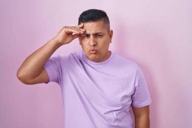 Young hispanic man standing over pink background worried and stressed about a problem with hand on forehead, nervous and anxious for crisis 
