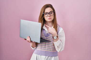 Young caucasian woman working using computer laptop pointing aside worried and nervous with forefinger, concerned and surprised expression 