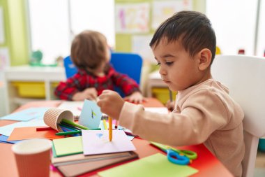 Two kids preschool students sitting on table drawing on paper at kindergarten