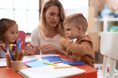 Teacher with boy and girl sitting on table having handcrafts class at kindergarten