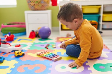 Anaokulunda yerde oturmuş ksilofon çalan sevimli beyaz çocuk.