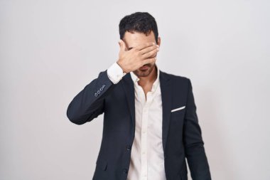 Handsome business hispanic man standing over white background covering eyes with hand, looking serious and sad. sightless, hiding and rejection concept 