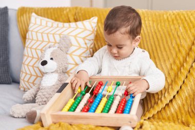 Tapılası İspanyol bebek, Abaküs ile oynuyor. Evdeki kanepede oturuyor.