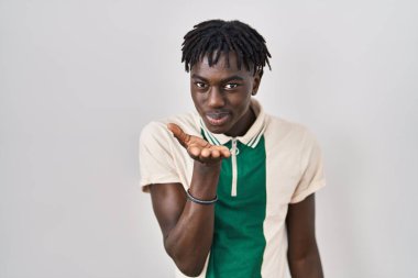 African man with dreadlocks standing over isolated background looking at the camera blowing a kiss with hand on air being lovely and sexy. love expression. 