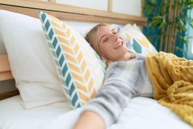 Genç sarışın kadın yatakta uzanıyor, yatak odasında uyuyor.