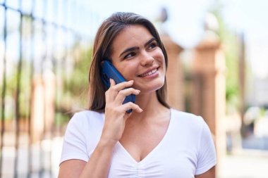 Gülümseyen genç bir kadın caddedeki akıllı telefondan konuşuyor.