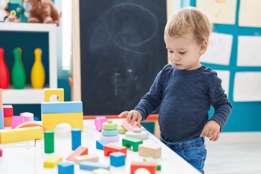 Anaokulunda duran sevimli sarışın çocuk geometri bloklarıyla oynuyor.