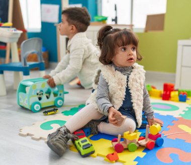 Brother and sister playing with cars toy sitting on floor at kindergarten