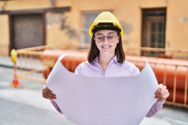 Young hispanic woman architect reading plans at street