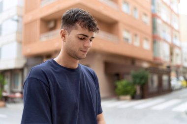 Latin kökenli genç adam ciddi bir ifadeyle sokağa bakıyor.