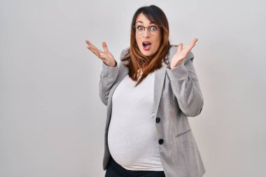 Pregnant business woman standing over white background celebrating victory with happy smile and winner expression with raised hands 