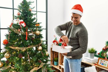 Genç İspanyol adam gülümsüyor. Evde kendine güvenen bir Noel ağacı süslüyordu.