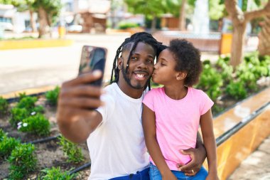 Baba ve kızı gülerek parkta akıllı telefondan özçekim yapıyorlar.