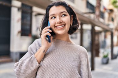 Gülümseyen genç bir kadın caddedeki akıllı telefondan konuşuyor.