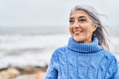 Middle age grey-haired woman smiling confident looking to the side at seaside