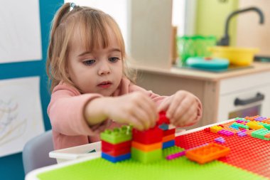 Adorable blonde girl playing with construction blocks sitting on table at kindergarten