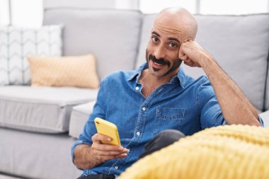 Genç İspanyol adam akıllı telefon kullanıyor. Evde yerde oturuyor.