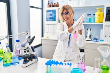 Middle age blonde woman working at scientist laboratory clapping and applauding happy and joyful, smiling proud hands together 