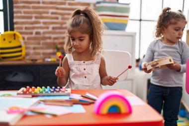 Anaokulunda masada oturmuş ksilofon oynayan iki çocuk.