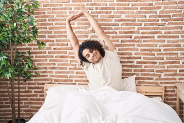 Genç latin adam yatak odasında kollarını esneterek uyanıyor.