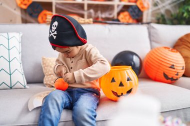 Adorable hispanic boy having halloween party holding pumpkin basket at home