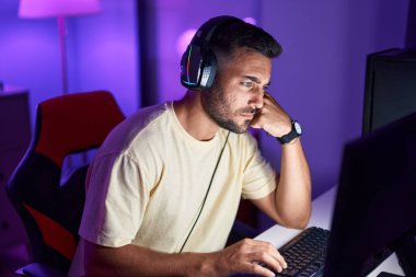 Oyun odasında ciddi bir ifadeyle masada oturan İspanyol asıllı genç adam.