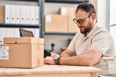 Genç Hispanik adam e-ticaret işçisi ofiste deftere yazıyor.