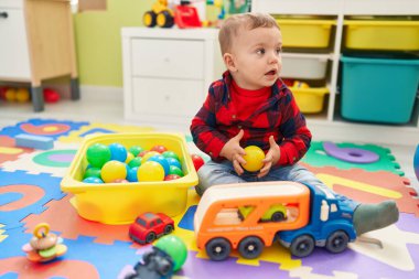 Anaokulunda yerde taşaklarıyla oynayan sevimli sarışın çocuk.