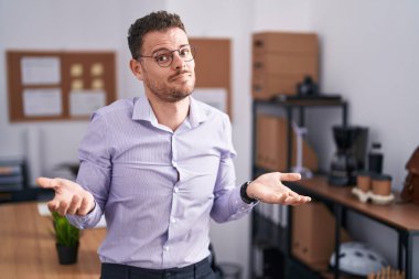 Young hispanic man at the office clueless and confused with open arms, no idea concept. 