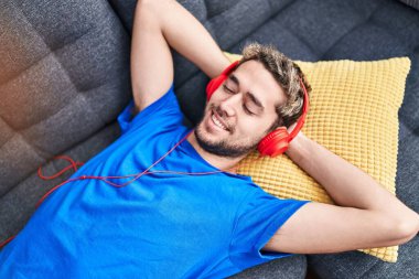 Young man listening to music lying on sofa at home