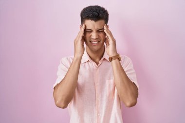 Pembe arka planda elleri başının üstünde duran genç İspanyol bir adam. Stres yüzünden başı ağrıyor. migren ağrısı. 