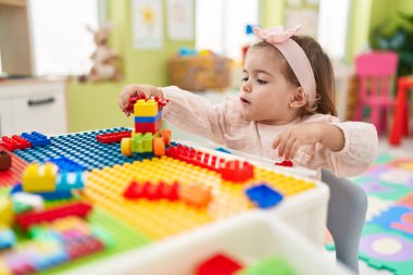 Anaokulundaki masada oturan sevimli sarışın çocuk inşaat bloklarıyla oynuyor.