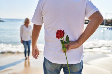 Middle age man and woman couple surprise with flower on back at seaside