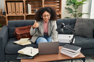 Young african american woman doing online session at consultation office smiling happy and positive, thumb up doing excellent and approval sign 
