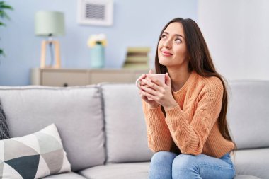 Genç ve güzel İspanyol kadın evdeki kanepede oturup kahve içiyor.