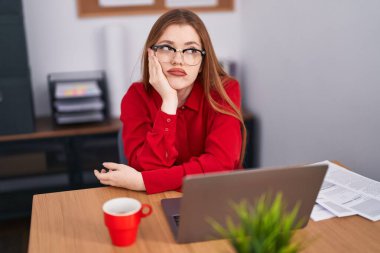 Young redhead woman business worker tired sitting on table at office