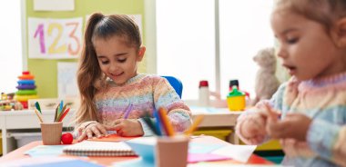 Two kids preschool students sitting on table drawing on paper at kindergarten