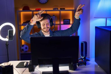 Beyazlı genç adam oyun odasında video oyunu oynuyor ve kazanan ifadesini kullanıyor.