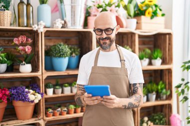 Young bald man florist smiling confident using touchpad at florist